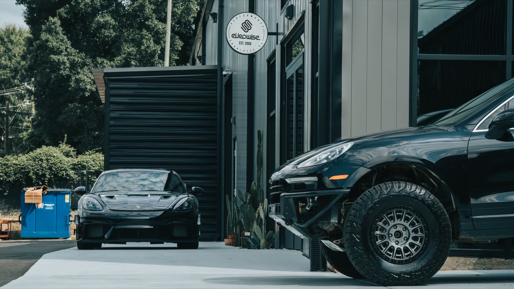 Black Porsche Cayenne and a sports car outside the shop