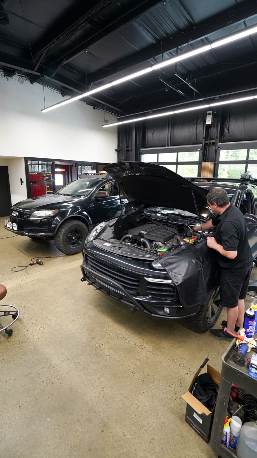 Technician working under the hood of a dark SUV