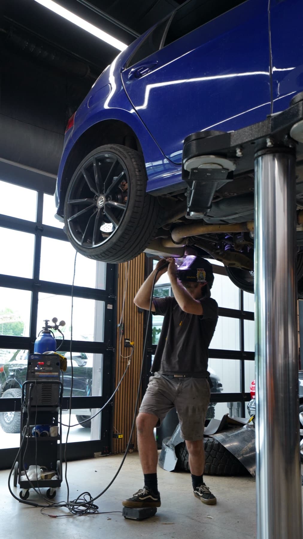 Technician working under a blue car raised on a lift