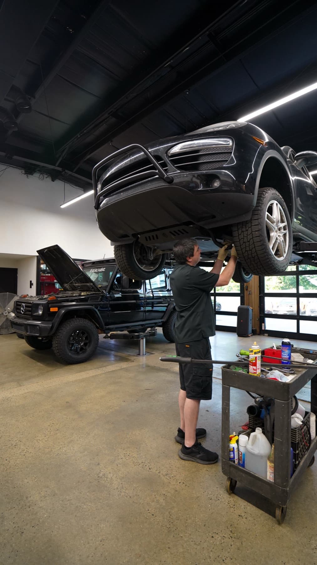Technician beside a dark SUV raised on a lift