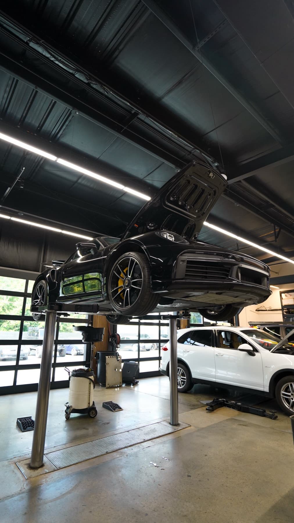 Dark car raised on a lift above a white SUV