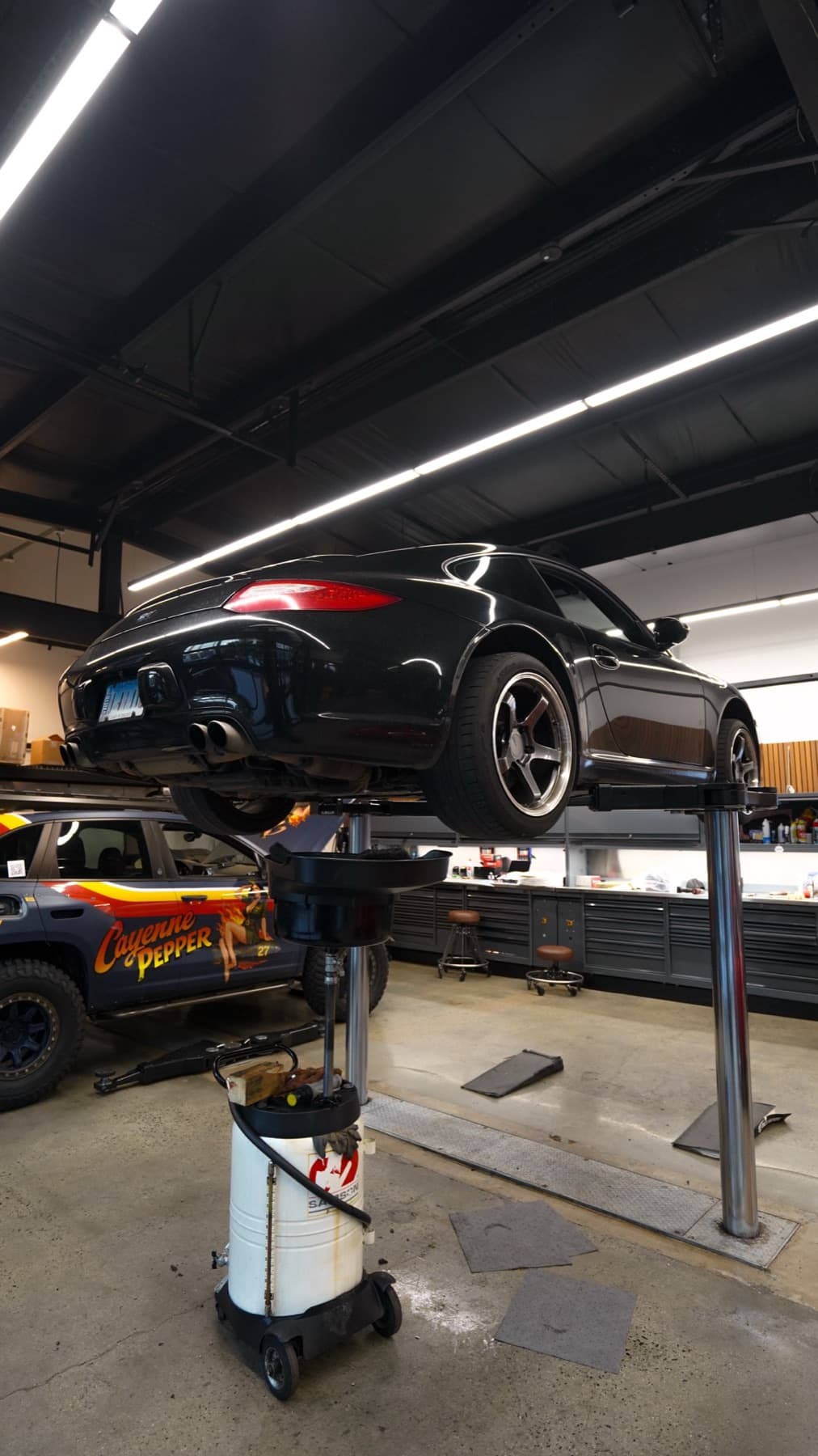Black Porsche on a lift with a white car below